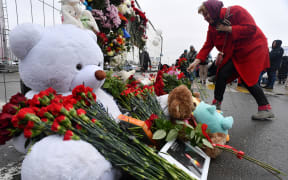 A woman lays flowers at a makeshift memorial in front of the Crocus City Hall, a day after a gun attack in Krasnogorsk, outside Moscow, on March 23, 2024. Camouflaged assailants opened fire at the packed Crocus City Hall in Moscow's northern suburb of Krasnogorsk on March 22, 2024, evening ahead of a concert by Soviet-era rock band Piknik in the deadliest attack in Russia for at least a decade. Russia on March 23, 2024, said it had arrested 11 people -- including four gunmen -- over the attack on a Moscow concert hall claimed by Islamic State, as the death toll rose to over 100 people. (Photo by Olga MALTSEVA / AFP)