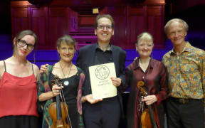Pianist Denes Varjon and the New Zealand String Quartet pose on stage following their performance of the Piano Quintet by Bela Bartok at the 2024 Adam Chamber Music Festival. Denes holds the score.