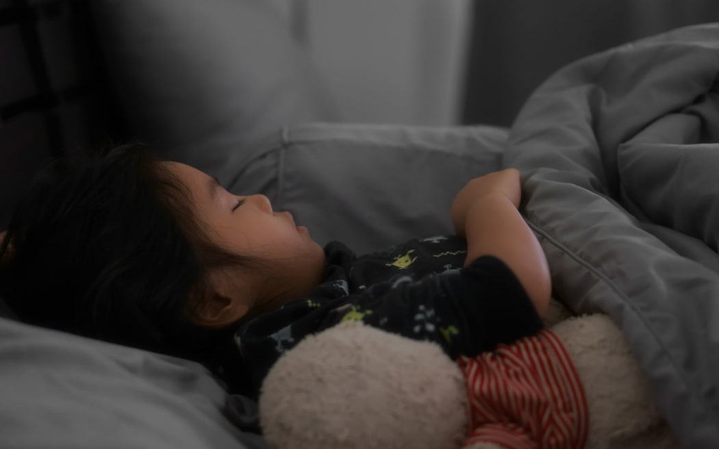 Child sleeping on grey dark bed