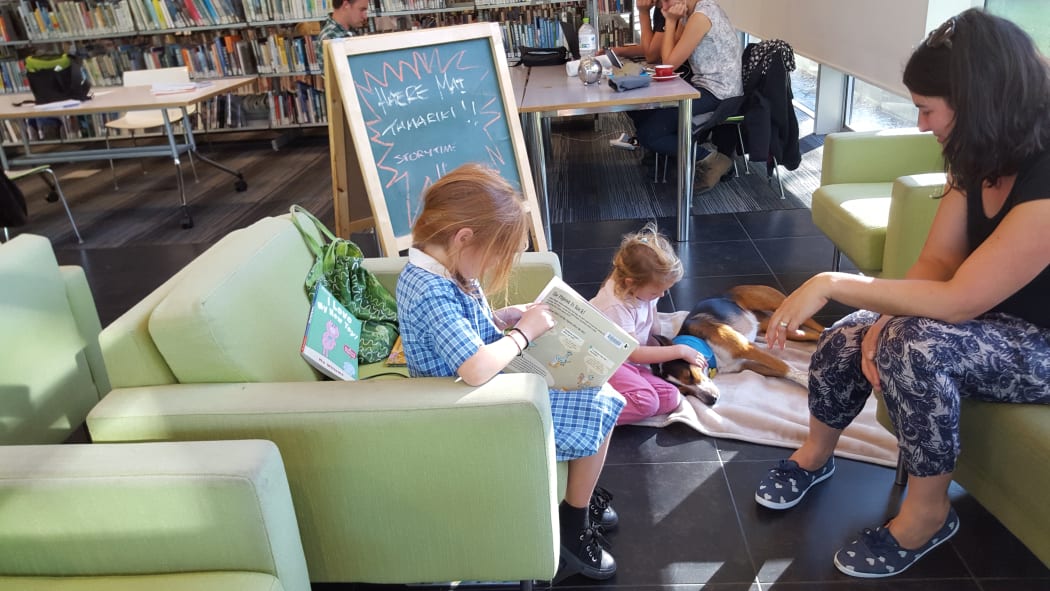 Zara,6, reads to Poppy the dog, while her sister Mila, 4, pats her.