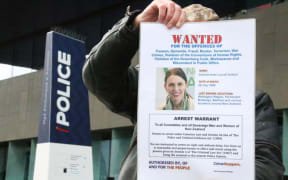 An anti-mandate protester outside Christchurch central police station holds up a fake arrest warrant for Prime Minister Jacinda Ardern.