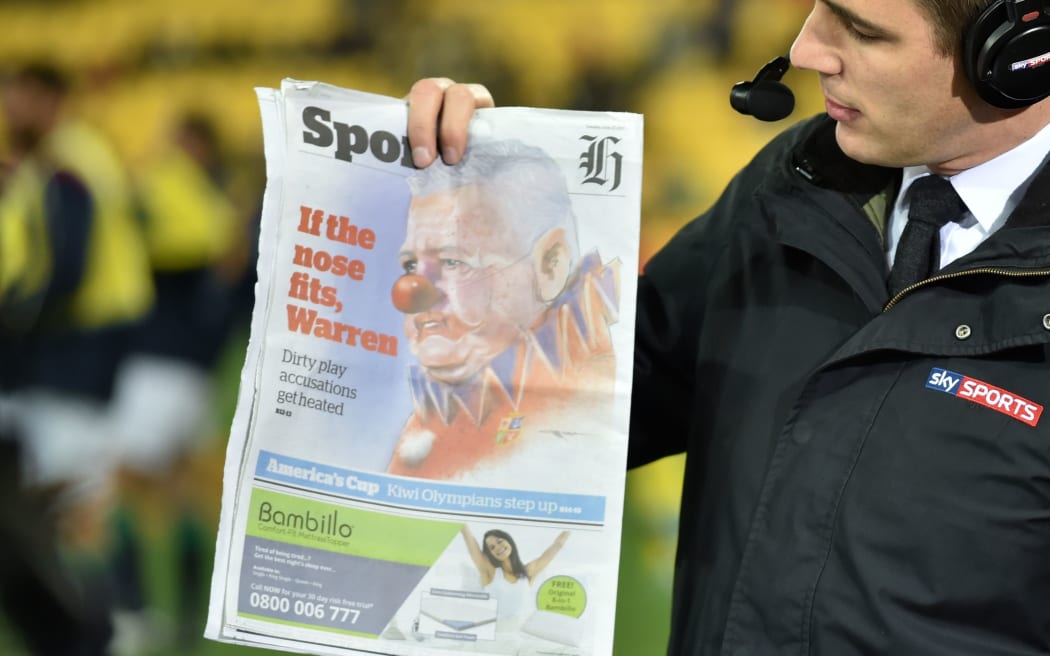 A television host holds up an image Lions coach Warren Gatland depicted as a clown before the Hurricanes game.