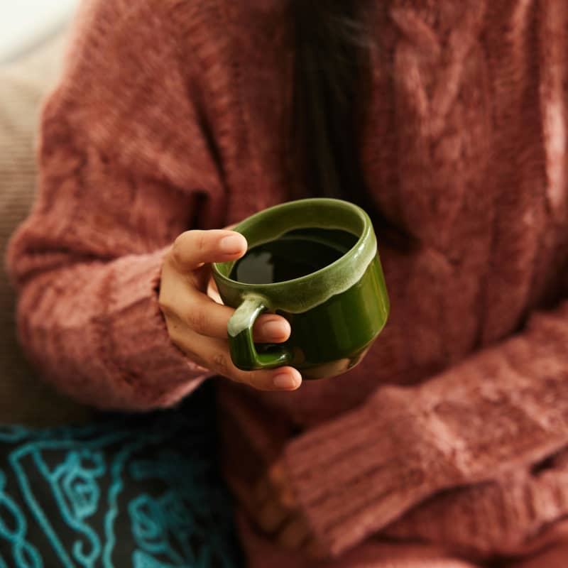A person in a brown sweater holds a green cup of water.