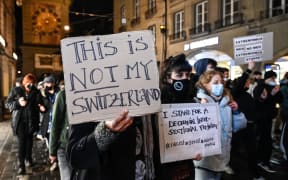 People hold signs during a protest hours after Switzerland has narrowly voted in favour of banning face coverings in public, including the burka or niqab worn by Muslim women.