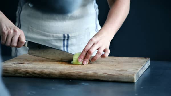 A person chops a cucumber on a wooden chopping board.
