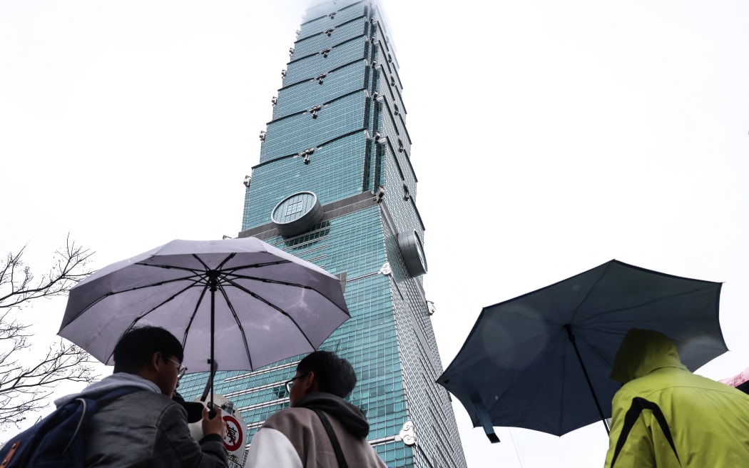 People hold umbrellas under the landmark Taipei 101 building, which US climber Alex Honnold was scheduled to scale but postponed due to bad weather, in Taipei on January 24, 2026. (Photo by I-Hwa Cheng / AFP)