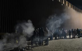 Asylum-seekers line up to be processed by US Customs and Border Patrol agents at a gap in the US-Mexico border fence near Somerton, Arizona, on 26 December, 2022.