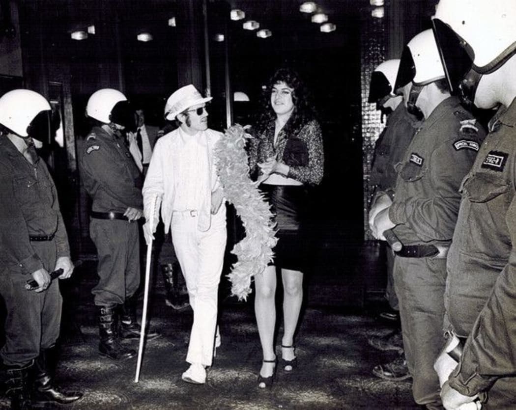 Neville Purvis and Cousin Cheryl - Arthur Baysting and Jean Clarkson - walk the police gauntlet to attend the premiere of 'Sleeping Dogs' at the Auckland Civic, 6 October 1977.