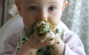 A photo of a toddler eating messy green food with her fingers
