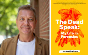 Thomas Coyle smiles at the camera. He wears a brown blazer and a white t-shirt.