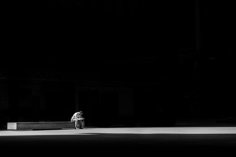 A man sitting alone on a bench. Black and white.