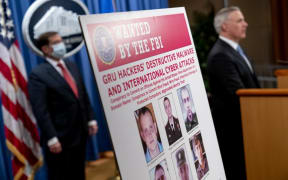 A poster showing six wanted Russian military intelligence officers is displayed as US Attorney for the Western District of Pennsylvania Scott Brady speaks at a news conference at the Department of Justice.