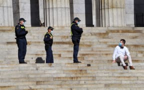 Protective Services officers speak to a man sitting on the steps of the Shrine of Remembrance in Melbourne on July 31, 2020.