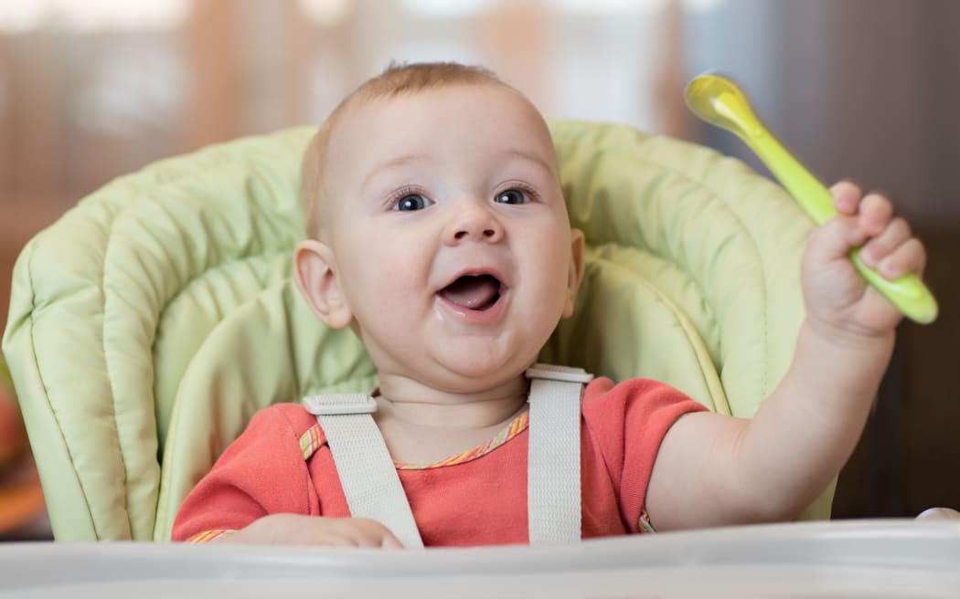Happy baby boy in high chair with spoon in his hand