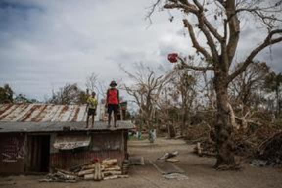 (Foreground) a child and an elderly man stand on the roof of a dwelling damaged Cyclone Pam, on Ifira Island, just off the coast of the main island of Efate.