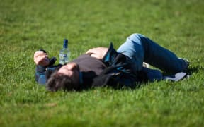 man lying in field with vodka bottle