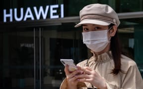 (FILES) In this file photo taken on May 25, 2020 a woman walks past a shop for Chinese telecoms giant Huawei in Beijing.
