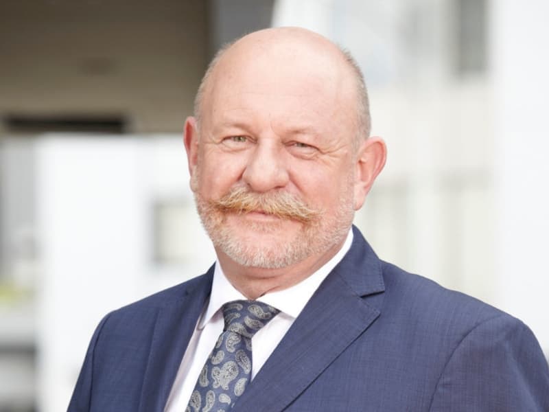 Mark Sainsbury is a softly smiling and balding man with a beard and long moustache.