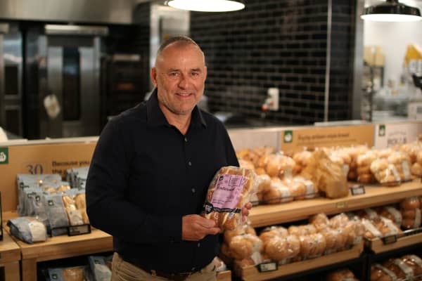 Michael Whorskey Woolworths NZ Merchandise Manager for Bakery, stands in front of  a bakery shelf holding a back of hot cross buns.