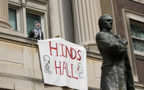 A pro-Palestinian student protester leans out a window of Hamilton Hall on the campus of Columbia University, April 30, 2024, in New York.