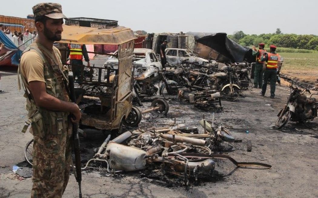 Pakistani soldiers stand guard beside burnt out vehicles at the scene where an oil tanker caught fire following an accident on a highway near the town of Ahmedpur East.