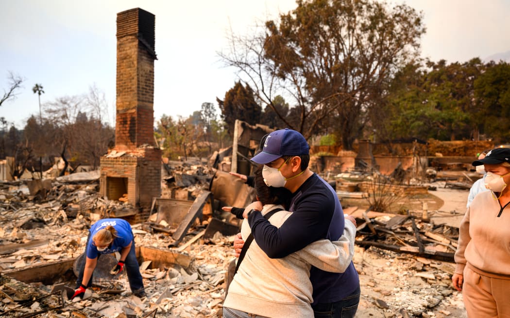Family members embrace while viewing their burned home during the Eaton fire in the Altadena area of Los Angeles county, California on January 9, 2025. Wildfires threatened to engulf parts of Hollywood on January 9 as a growing number of blazes raged across Los Angeles, forcing over 100,000 people to flee their homes and claiming at least five lives. (Photo by JOSH EDELSON / AFP)