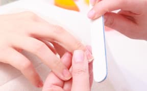 Beautician with file filing nails female client. Woman spa beauty salon