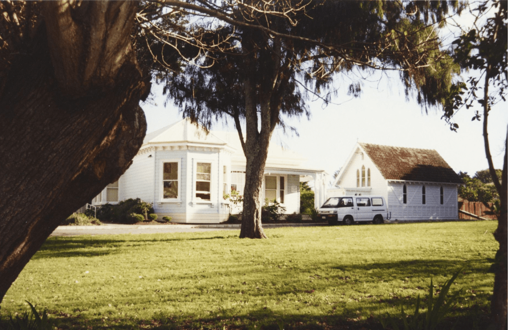 View of St Mary's Family Home, Great South Road, Ōtāhuhu, June 1998. St Mary's Women's Home was originally opened as an Anglican home for unwed mothers on 25 March 1904. The villa to the left was one of the original two buildings. The Chapel of St Mary Magdeline, to the right, was dedicated on 31 May 1911. In 1983 the complex was renamed St Mary's Family Home. This underlined its expanded functions as a social centre for mothers and children, by now not only operating home units for mothers and babies, but also providing a day-care centre, family counselling services, play groups, baby-care and budgeting and home management programmes.