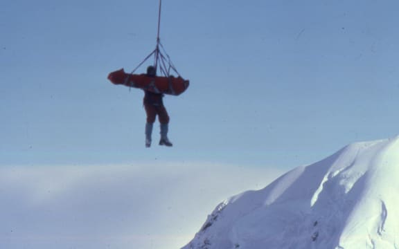 A photo of Don Bogie hanging from the helicopter with Mark Inglis attached to him in a soft stretcher known as a Bauman Bag