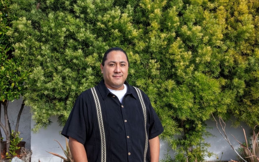Frankie Guzman stands in front of a concrete wall covered in green plants. He's smiling at the camera.