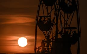People enjoy a ferris wheel ride as the moon partially obscures the sun during a partial solar eclipse visible from Chennai on 25 October, 2022.