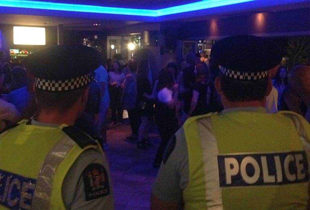 Two police officers in uniform look on as clients dance at night in bar
