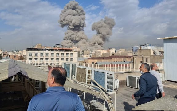 People watch as smoke rises on the skyline after an explosion in Tehran, Iran on February 28, 2026.