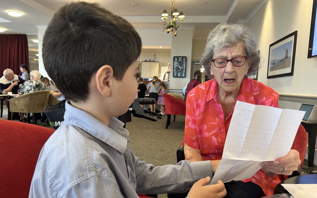 Photo of an elderly woman helping a child reading a letter.