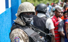 Police look on as a crowd surrounds the Petionville Police station.