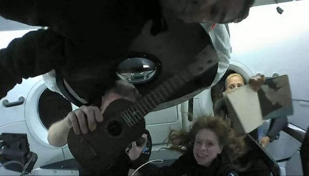 This screengrab taken from the SpaceX live webcast on September 17, 2021 shows Inspiration4 crew members (from L) Jared Isaacman, Christopher Sembroski holding up a ukelele, Hayley Arceneaux and Sian Proctor holding up her artwork while in orbit.
