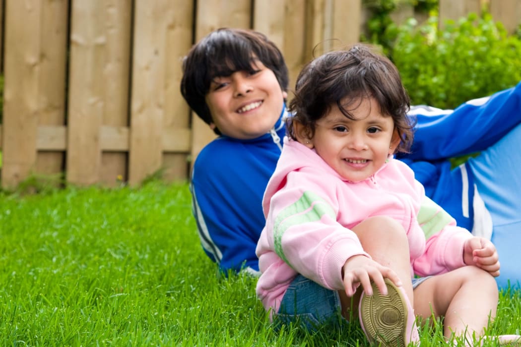 A photo of a young boy sitting in the backyard with his sister