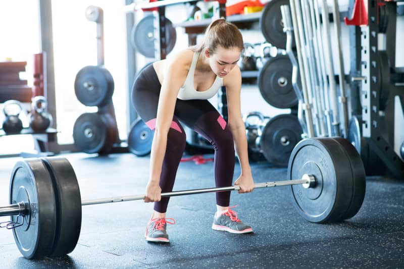 A young woman lifts a heavy looking barbell.
