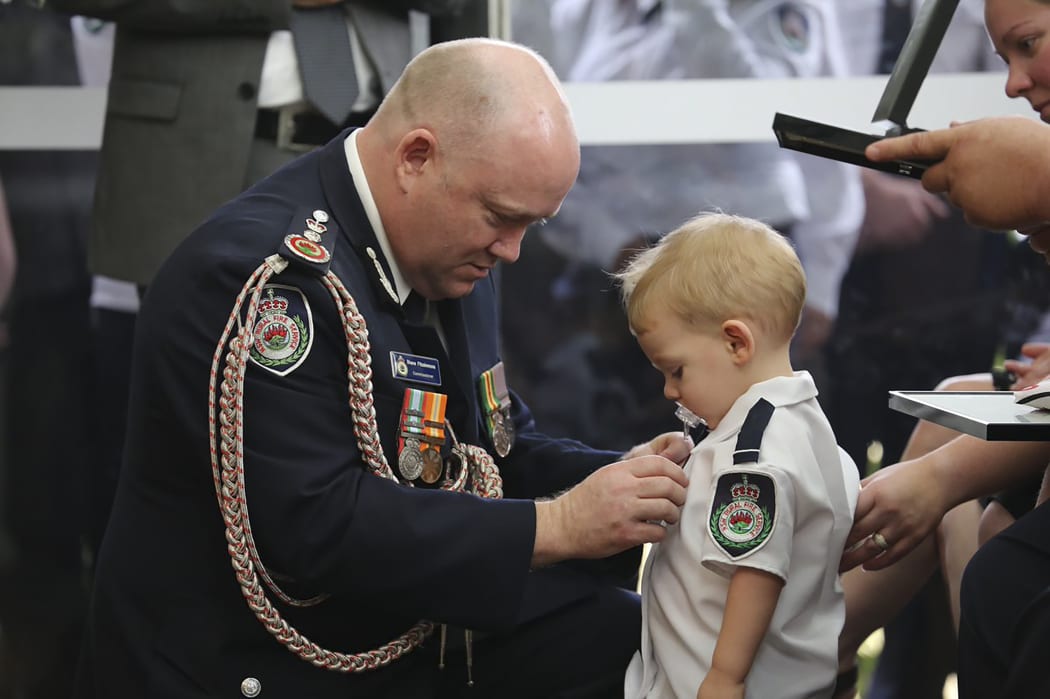 Australian Rural Fire Service Commissioner Shane Fitzsimmons pinning a medal on Geoffrey Keaton's son Harvey.