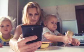 mother looking at mobile phone while with two children