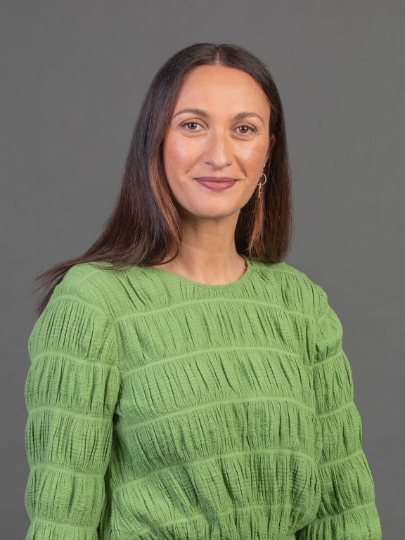 Kara Rikard stands in a studio on a grey backdrop in a green top