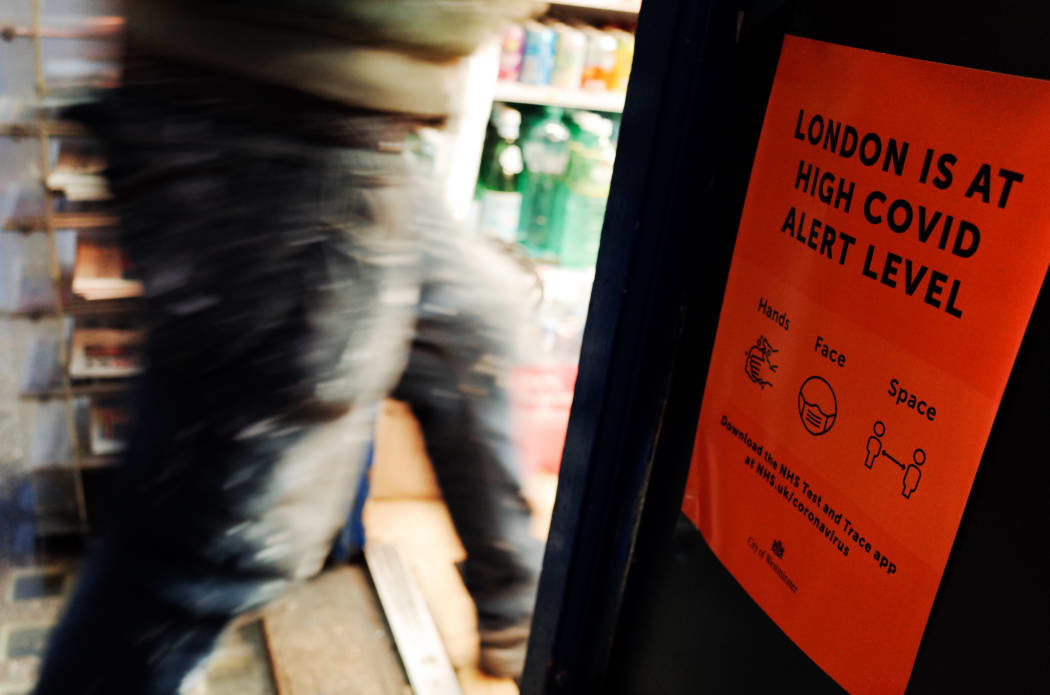 A man passes a notice warning of the current 'high' alert level for covid-19, taped at the entrance to a newsagent on Old Compton Street in Soho in London, England