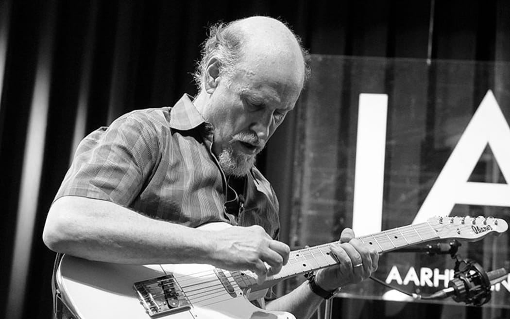 A black and white photo of John Scofield looking down at his guitar as he plays.