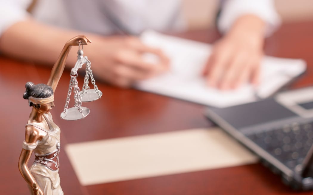 Follow the law. Professional lawyer sitting at the table and signing papers with justice statue standing on surface in forefront.