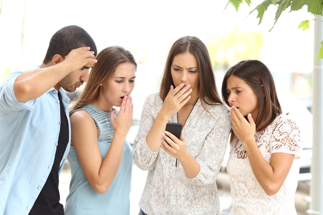 A photo of four worried multi ethnic friends watching a smart phone in the street