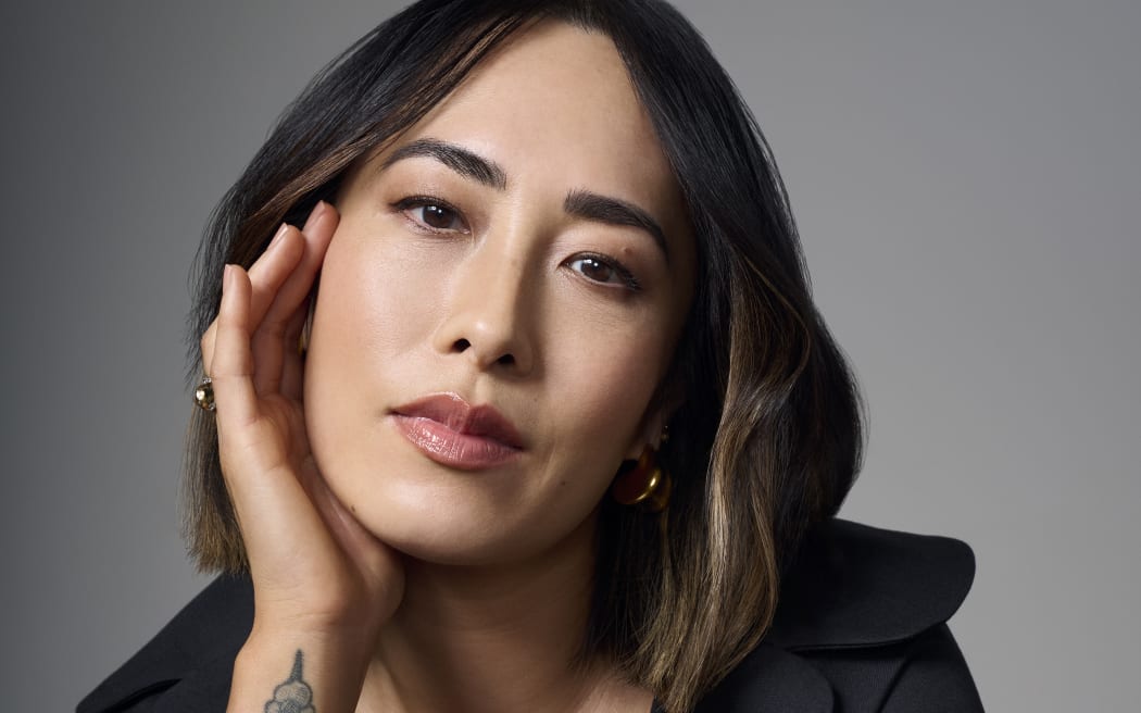 Melissa Leong, a 43 year old Asian woman with a shoulder length bob, cups her face with one hand and stares at the camera.