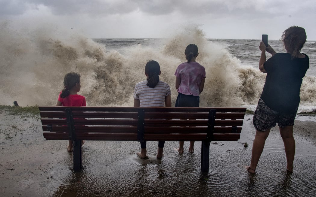 A family watch the storm roll in across the Coral Sea at Holloways Beach as Cyclone Jasper approaches landfall in Cairns in far north Queensland on December 13, 2023. A tropical cyclone was building strength as it rolled towards northeastern Australia on 13 December, with authorities warning "life-threatening" floods could swamp coastal regions for days. (Photo by Brian CASSEY / AFP)