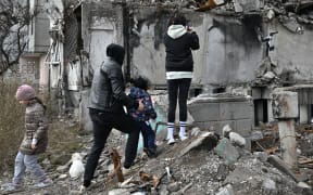 Local residents look at a graffiti made by Banksy on the wall of a destroyed building in Borodyanka, near Kyiv on November 12, 2022, amid the Russian invasion of Ukraine. Banksy, the elusive British street artist, has painted a mural on a bombed-out building outside Ukraine's capital, in what Ukrainians have hailed as a symbol of their country's invincibility. On November 11's night the world-famous graffiti artist posted on Instagram three images of the artwork -- a gymnast performing a handstand amid the ruins of a demolished building in the town of Borodyanka northwest of the Ukrainian capital Kyiv. (Photo by Genya SAVILOV / AFP) / RESTRICTED TO EDITORIAL USE - MANDATORY MENTION OF THE ARTIST UPON PUBLICATION - TO ILLUSTRATE THE EVENT AS SPECIFIED IN THE CAPTION