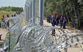 Migrants and refugees walk near razor-wire along a three-meter-high fence secured by Hungarian police at the official border crossing between Serbia and Hungary.