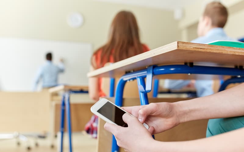 A student texting in a classroom under his desk during a lesson.